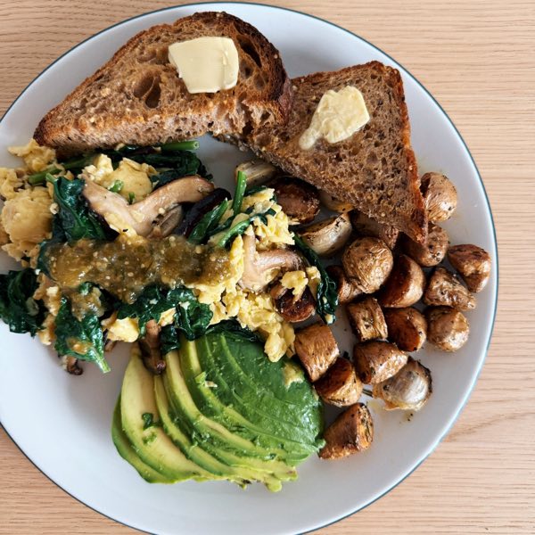 Scrambled eggs with greens and mushrooms, roast potatoes, avocado and buttered toast.
