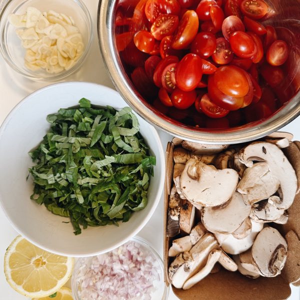 Halved cherry tomatoes, shredded basil, sliced mushrooms, garlic and shallots in bowls.