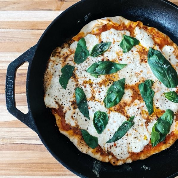 A cast-iron skillet pizza topped with mozzarella and fresh basil.
